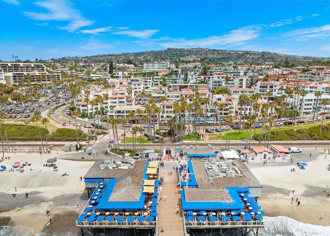 Aerial view of the pier restaurants with blue umbrella decks over the sand and surf