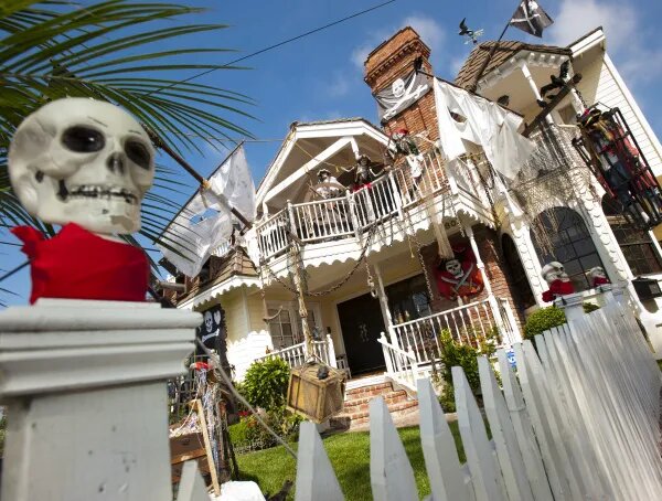 House decorated for Halloween with skeleton pirates, flags and a large skull on a white picket fence post