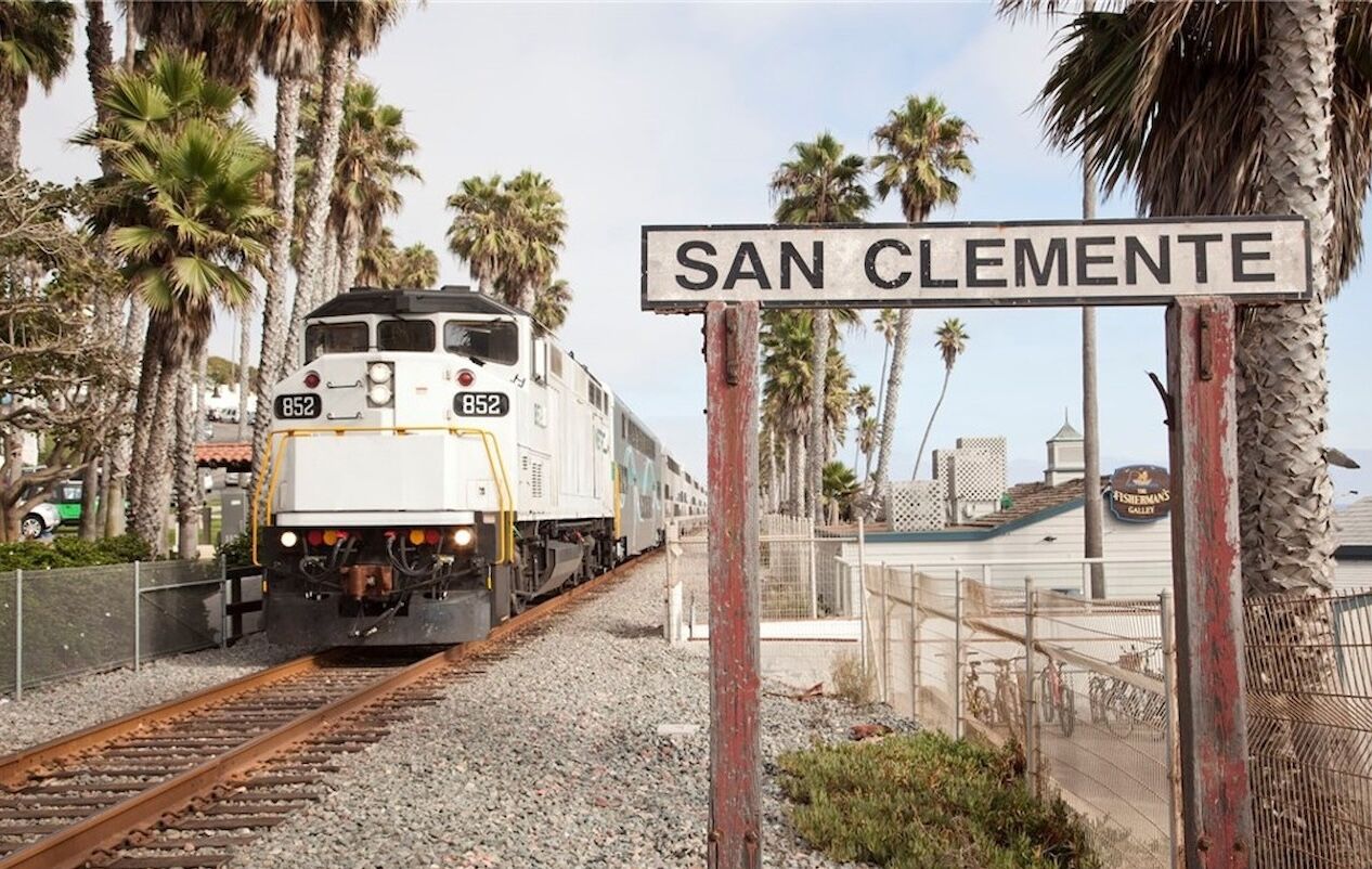 Train passing the San Clemente station sign beside palm trees