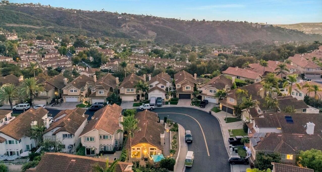 Aerial view of tile-roof homes along curving streets with hills behind at dusk in San Clemente