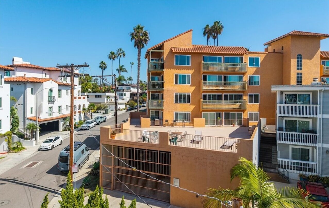 Terracotta-colored coastal condominium building with balconies and palm trees on a San Clemente street