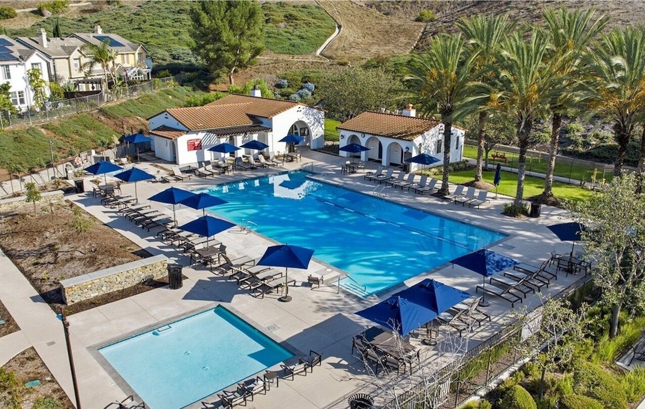 Aerial view of a community pool, spa and Spanish-style cabanas with blue umbrellas beside hillside homes