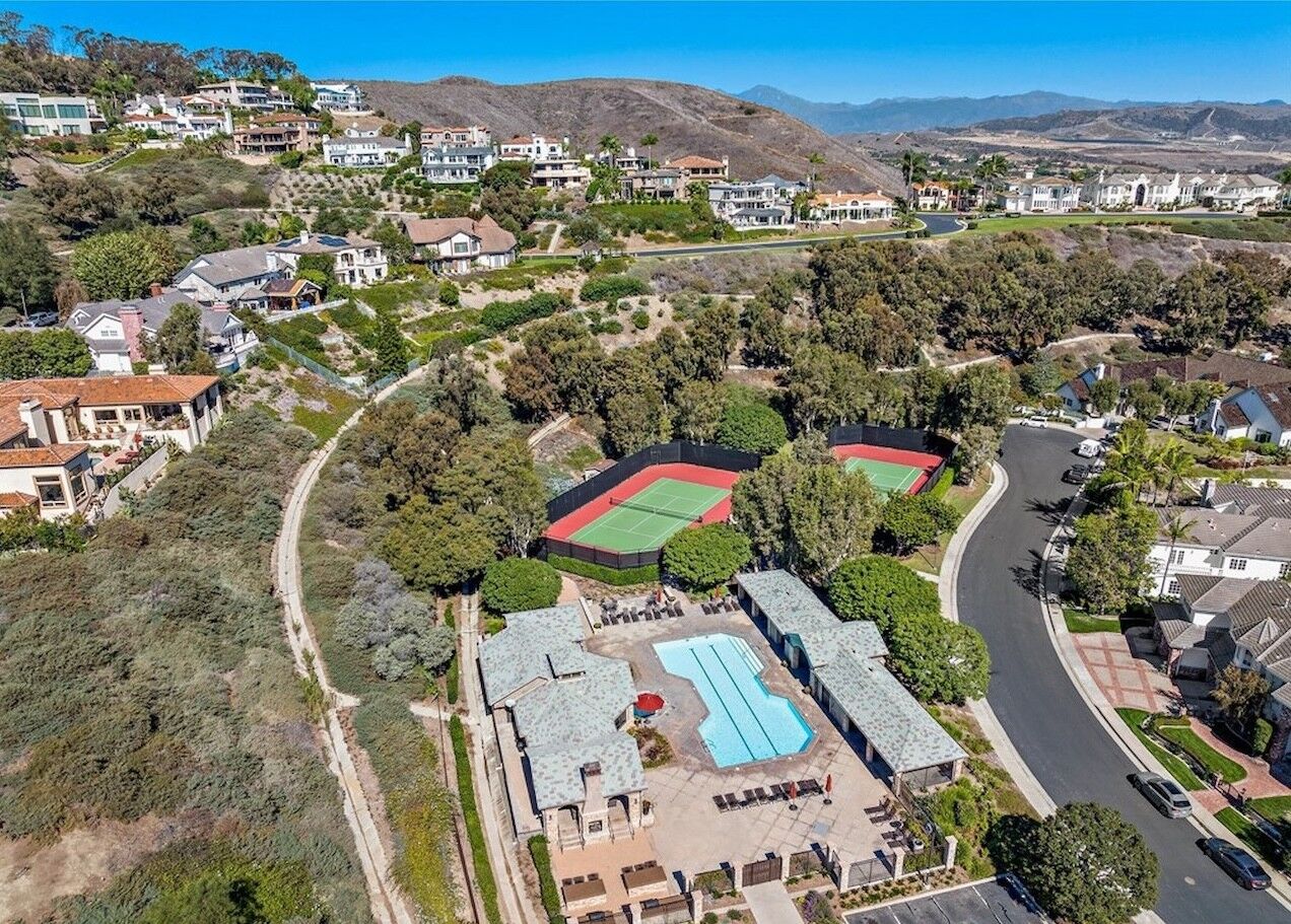 Aerial view of a community clubhouse, pool and tennis courts among hillside homes