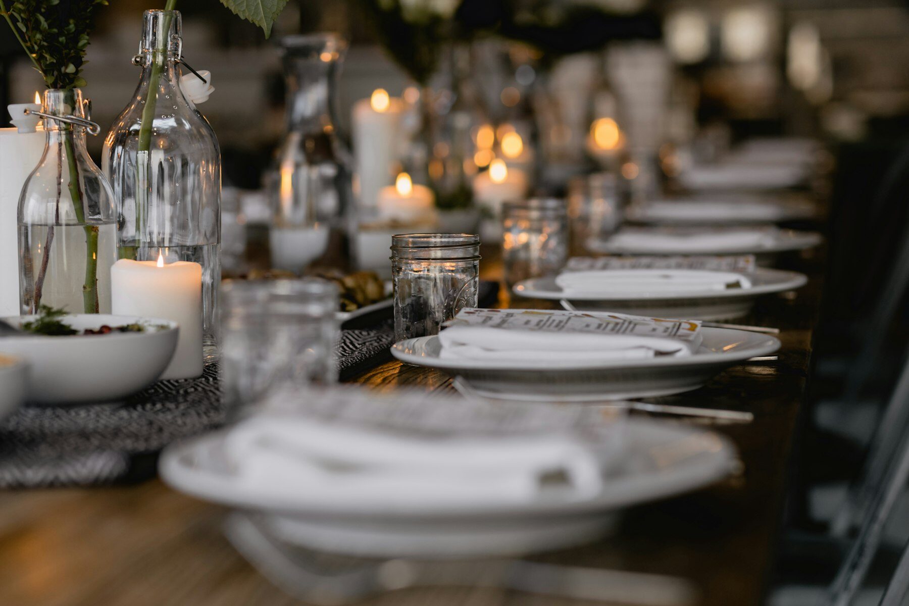 Long dinner table set with white plates, napkins, glassware and lit candles