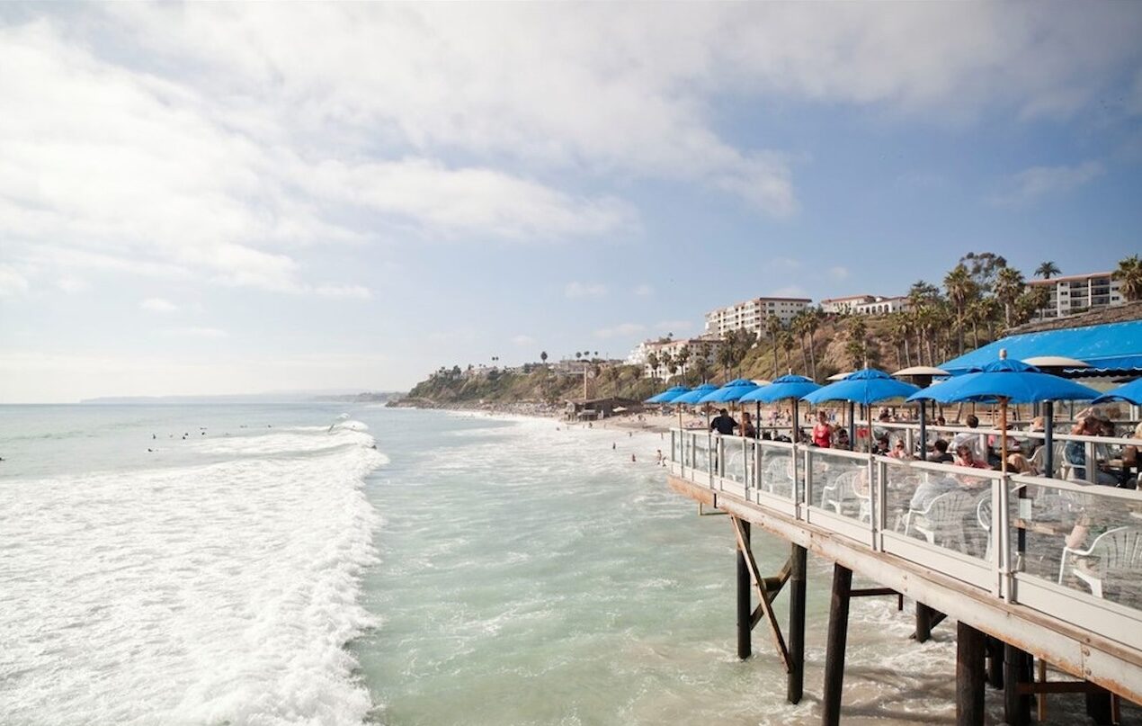Oceanfront pier restaurant deck with blue umbrellas above the surf in San Clemente