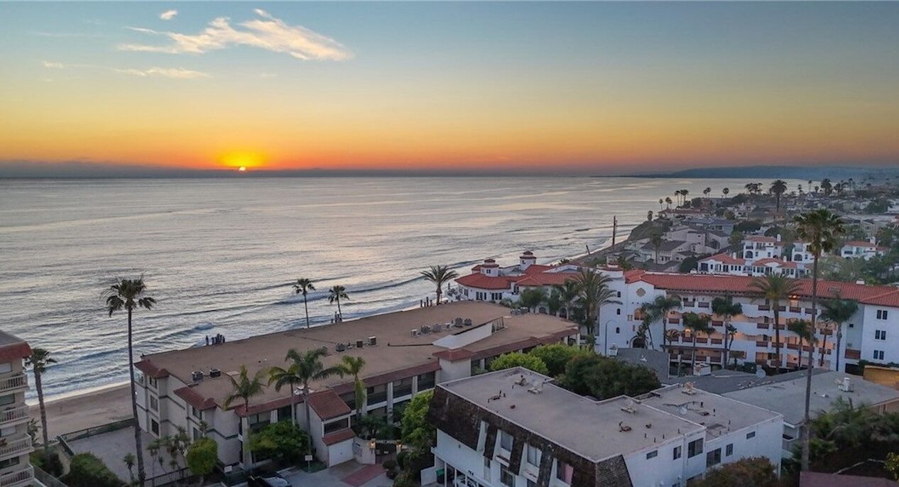 Sunset over the Pacific Ocean beside oceanfront buildings with red tile roofs and palm trees in San Clemente
