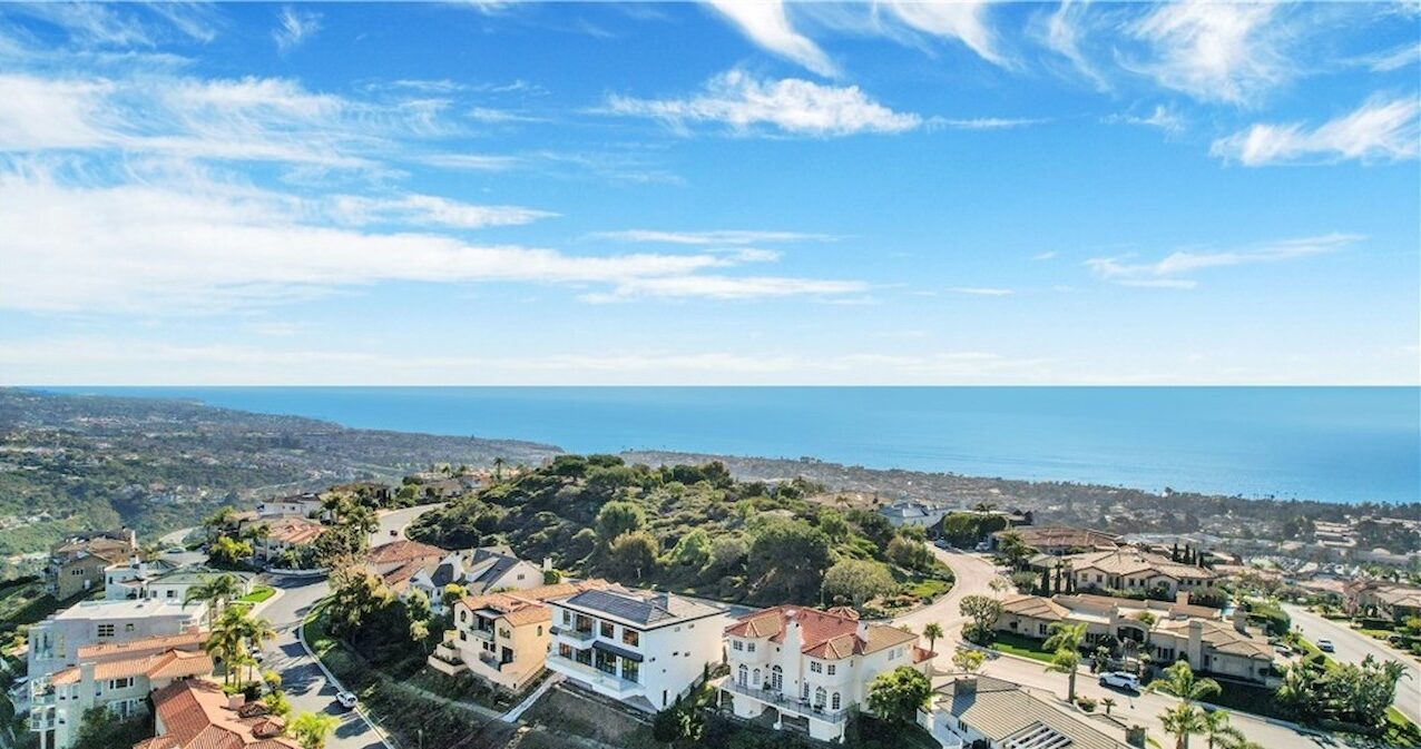 Aerial view of hillside homes with the Pacific Ocean stretching out below under a bright sky in San Clemente
