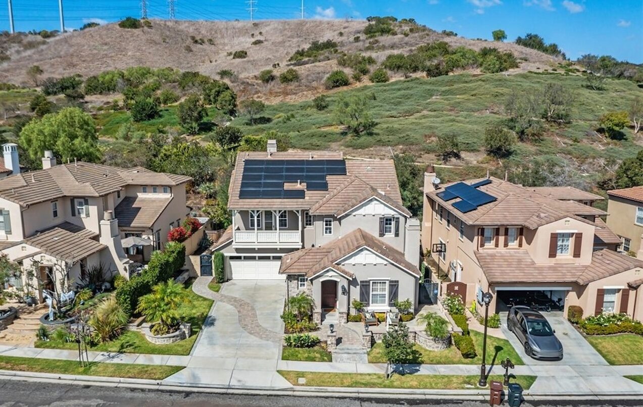 Aerial view of two-story homes with solar panels and open hillside behind in Talega, San Clemente