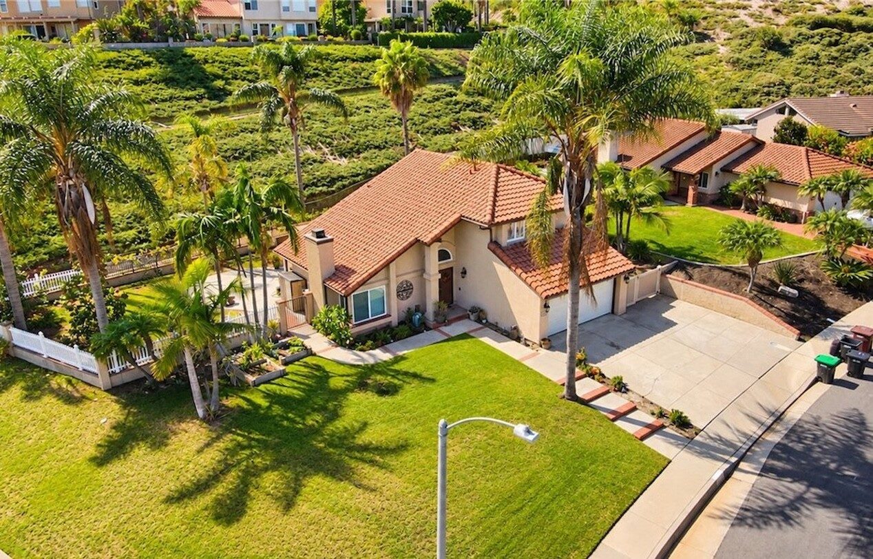 Single-story tile-roof home with a lawn and palm trees on a corner lot in San Clemente